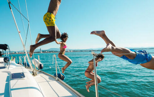 Happy friends diving from sailing boat into the sea - Focus on left girl face right man face